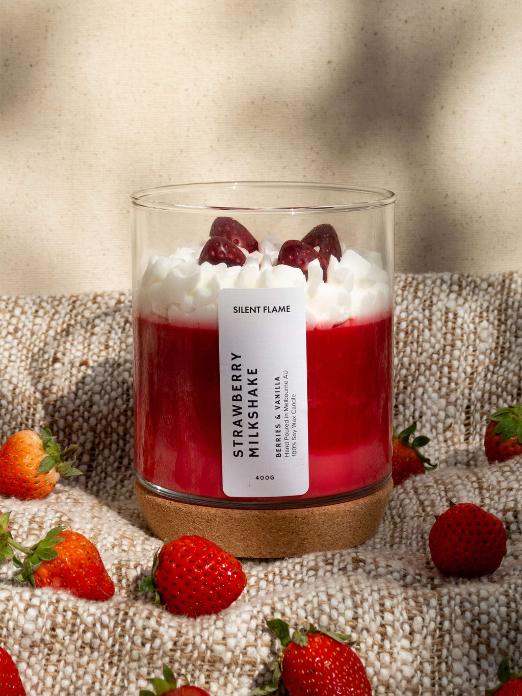 Candle labeled 'Strawberry Milkshake' with strawberries around on a textured surface