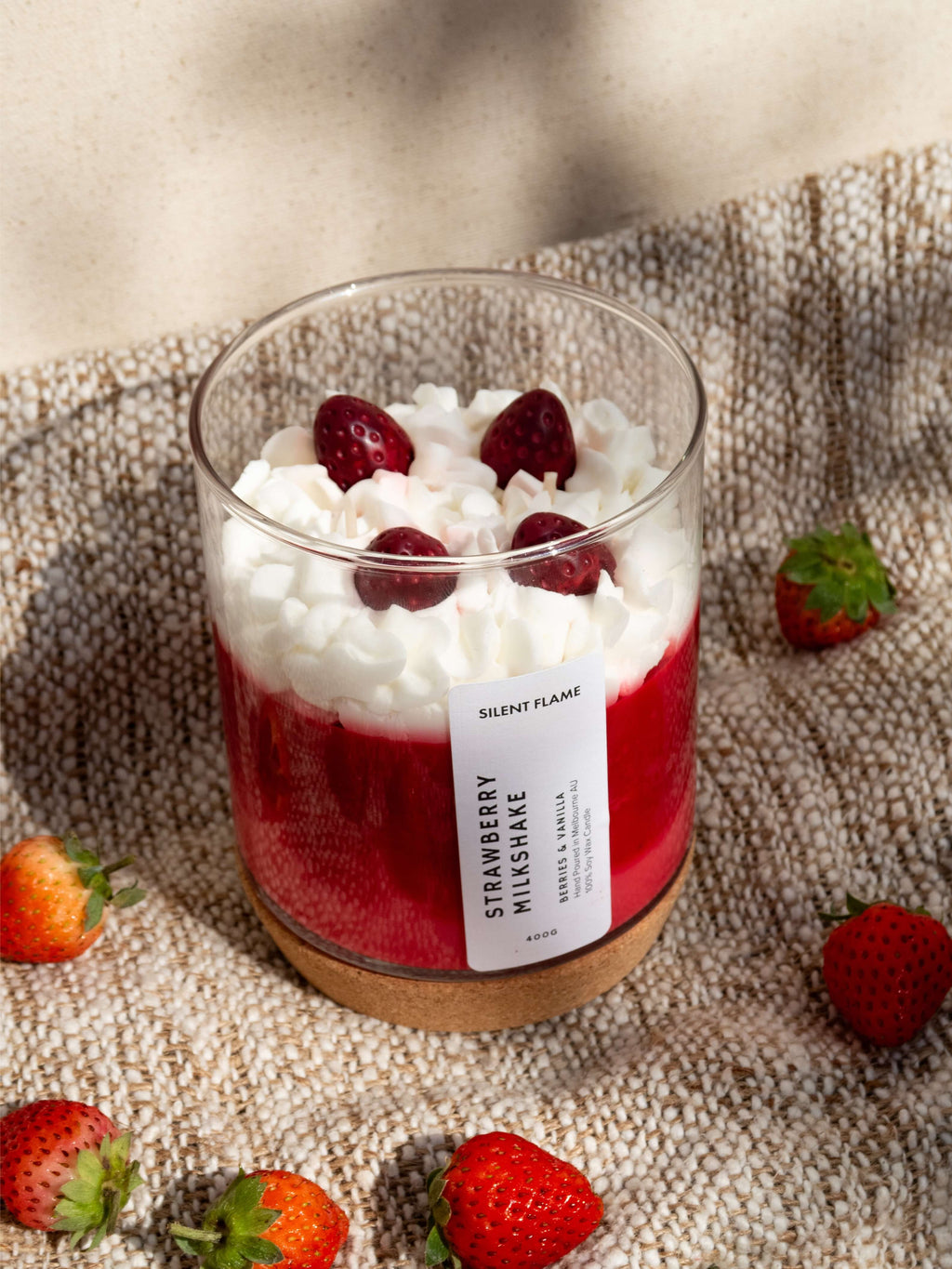 Candle in a glass jar with strawberries and cream on a textured surface