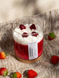 Candle in a glass jar with strawberries and cream on a textured surface