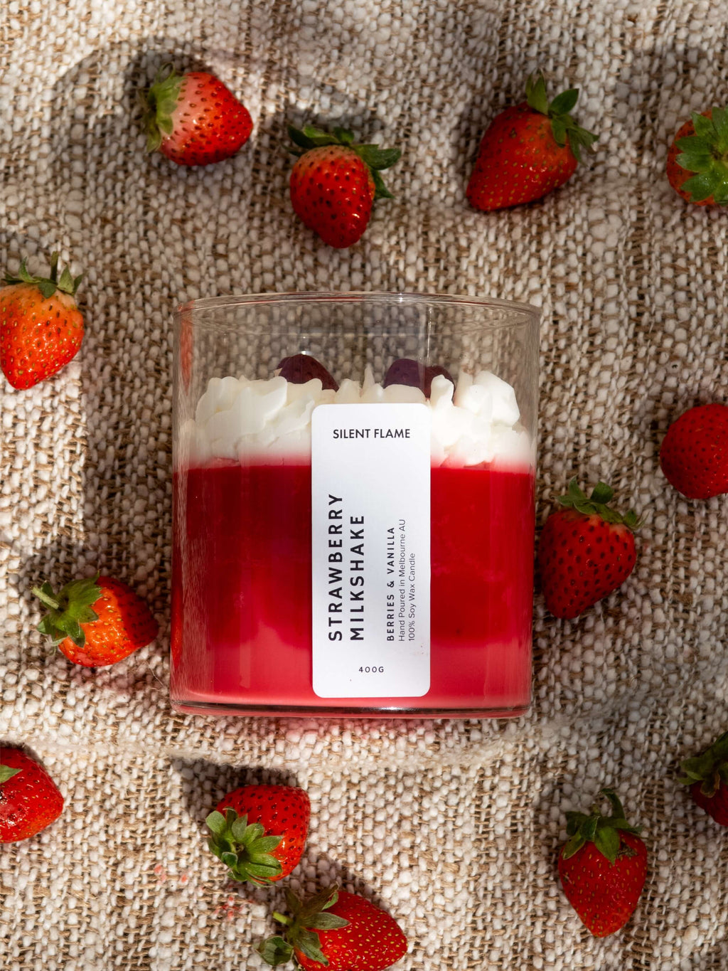 Candle labeled 'Strawberry Milkshake' surrounded by strawberries on a textured surface